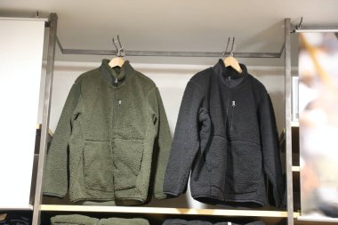 Bir askıda asılı iki ceket, biri yeşil diğeri siyah. Ceketler tüylü bir malzemeden yapılmış ve fermuarları var.