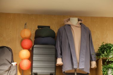 A mannequin is wearing a gray jacket and a hoodie. A black suitcase is next to the mannequin clipart