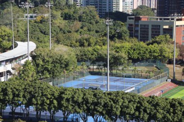 Arkasında bir sürü ağaç ve birkaç bina olan bir park. Parkta birkaç tenis kortu var.