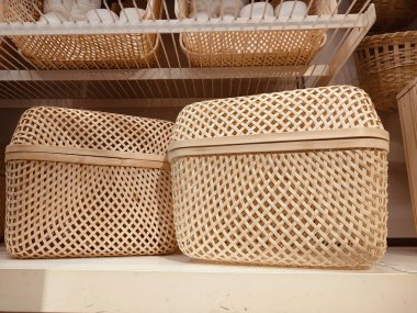 Bir rafta iki sepet örülmüş sepet var. Sepetler tahtadan yapılmış ve kafes tasarımları var.