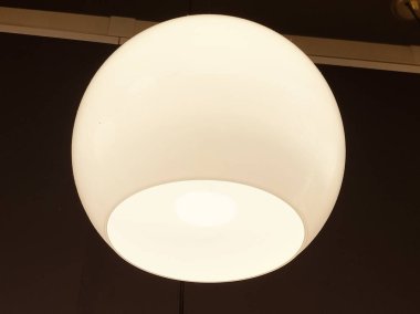 Tavandan sarkan yuvarlak, beyaz bir ampul, odayı yumuşak, sıcak bir ışıltıyla aydınlatıyor.