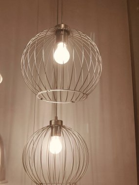 İçinde tel çerçeve ve ampul olan gümüş bir lamba. Işık açık ve lamba tavandan sarkıyor.