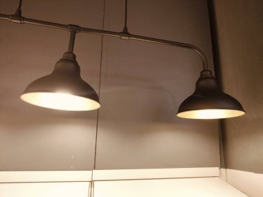 Tavandan sarkan sarı ışıklı iki siyah lamba. Lambalar gri bir duvarda.