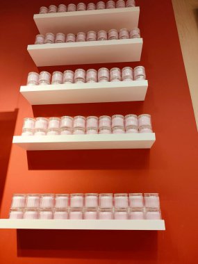 Üzerinde pembe mumlar olan bir sıra raf. Mumlar temiz cam kavanozlarda ve düzenli ve düzenli bir şekilde düzenlenmiş. Raflar beyaz ve arka plan kırmızı.