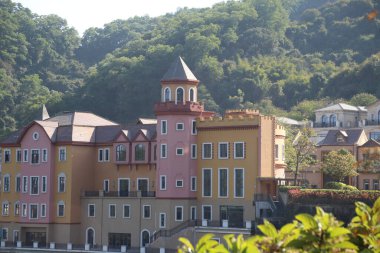 Kırmızı çatılı ve sarı renkli binalardan oluşan bir sıra. Binalar arka planında yeşil bir tepe olan bir kasabada.