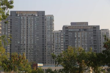Önünde bir sürü penceresi ve yeşil ağacı olan büyük bir bina. Bina gri ve modern görünümlü.