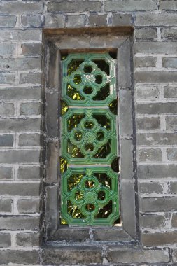 Yeşil çerçeveli ve yeşil desenli bir pencere. Pencere tuğla bir duvarda. Pencere açık ve güneş parlıyor.