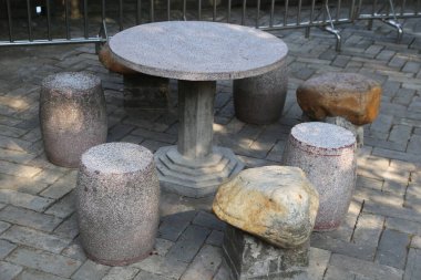 Beş taş koltuklu ve ortasında bir taş olan taş bir masa. Masa çitlerle çevrili.