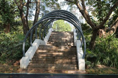 Köprüye çıkan metal bir merdiven. Köprü kıvrımlı ve metal parmaklıkları var. Merdivenler betondan yapılmış ve yosunla kaplı. Köprü ve merdivenler ağaçlarla çevrili.