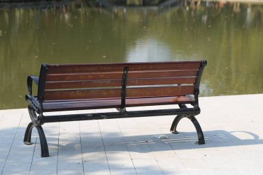 Tahta bir bank kaldırımda bir su kütlesinin yanında oturur. Bankta kimse yok ve o huzurlu bir ortamda.