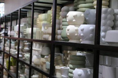 Bir sıra beyaz ve yeşil vazo bir rafa dizilmiştir. Vazolar çeşitli şekil ve boyutlarda ve hepsi beyaz.