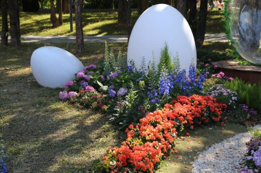 Büyük beyaz bir yumurtası ve küçük beyaz bir yumurtası olan bir bahçe. Bahçe renkli çiçekler ve bitkilerle dolu.