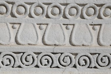 Taştan yapılmış dekoratif bir kenarı olan beyaz bir duvar. Kenar, daireler ve üçgenler de dahil olmak üzere çeşitli şekillerden oluşur ve oldukça karmaşıktır. Sahne zarafet ve entelektüelliktir.
