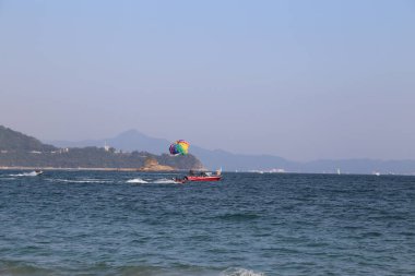 Bir grup insan okyanus üzerinde paraşütle atlıyor. Gökyüzü açık ve su sakin.