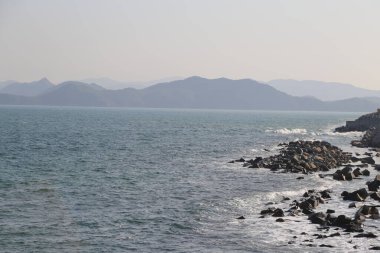 Okyanus sakin ve gökyüzü açık. Arka plandaki dağlar huzur ve huzur hissi yaratıyor.