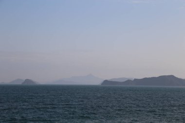 Okyanus sakin ve gökyüzü açık. Arkadaki dağlar karla kaplı.