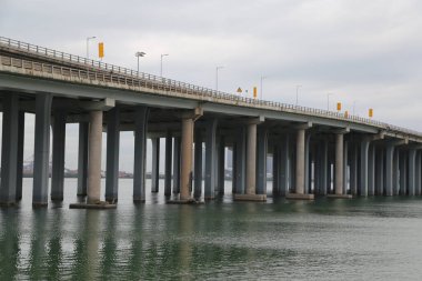 Köprü, köprünün üzerinde birkaç sarı ışık bulunan bir su kütlesini kapsar. Köprü uzun ve gri renkli.