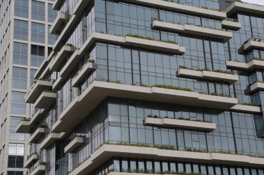 Yeşil çatılı ve balkonlu yüksek bir bina. Bina camdan yapılmış ve modern bir tasarımı var.