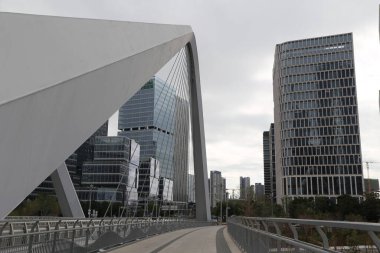 Bir köprü iki yüksek bina arasındaki bir nehri kapsar. Köprü beyaz ve üçgen şeklinde. Binalar yüksek ve birçok pencereleri var. Gökyüzü bulutlu ve sahne şehirli.