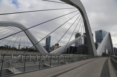 Bir köprü, arka planda yüksek binalar olan bir şehirde bir nehri kapsar. Köprü geniştir ve bir sürü metali vardır.