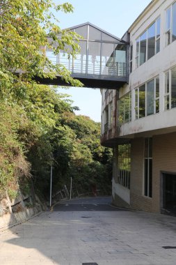 Cam yolu olan bir bina ve arka planda yeşil bir tepe. Geçit ağaçlarla çevrili ve bina beyaz.