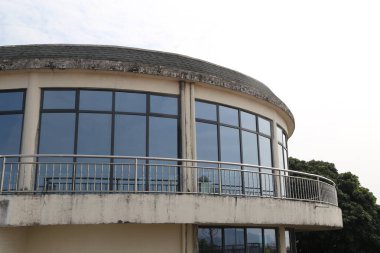 Cam çatılı ve balkonlu büyük bir bina. Bina beyaz ve dairesel bir şekli var.