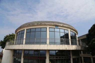 Dairesel tasarımı ve bir sürü penceresi olan büyük bir bina. Bina ağaçlarla çevrili ve modern görünümlü.