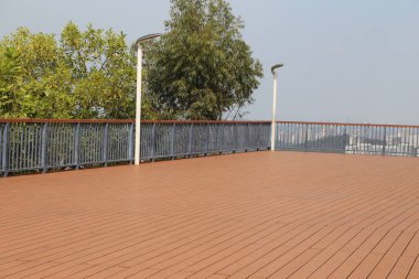 Korkuluklu ve arka planda ağaç olan tahta bir güverte. Güverte boş ve korkuluklar mavi.