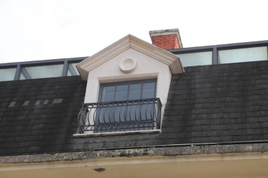 Binanın üstünde balkon olan bir pencere. Balkon siyah ve pencere beyaz. Binanın çatısı siyah.