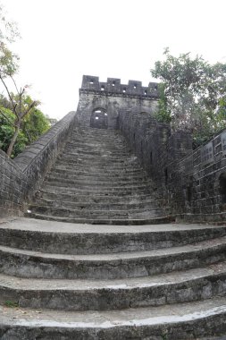 Kaleye çıkan taş bir merdiven. Basamaklar aşınmış ve taş gri. Kale arka planda ve merdivenler kalenin tepesine çıkıyor.