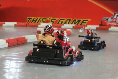 Bir grup insan bir pistte go kart yarışıyor. Pist kırmızı ve beyaz. Üzerinde 