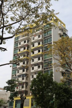 Bir sürü penceresi ve balkonu olan uzun sarı bir bina. Bina ağaçlarla çevrili ve bir sürü balkonu var.