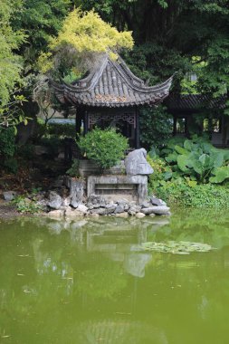 Ortasında duvar ve pagoda olan küçük bir gölet. Gölet yeşil ve sakindir.