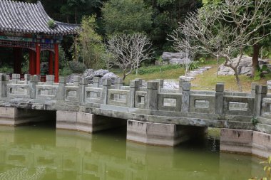 Kırmızı çatılı ve taş duvarlı bir göletin üzerinde bir köprü. Köprü taştan yapılmıştır ve yanında taş bir duvar vardır. Gölet yeşil ve sakindir.