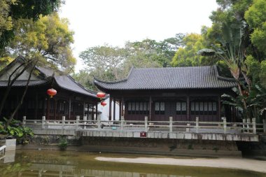 Parkta, bir tarafında koyu ahşap oymalar ve beyaz duvarlar olan antik bir Çin tarzı bina var. Şunun yanında da tahta bir yapı var, saçaklarından kırmızı fenerler sarkan..