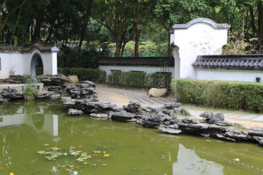 Yeşil ağaçları, kayalıkları ve alçak duvarlarla çevrili bir parkın köşesindeki göleti olan beyaz, Çin tarzı bir bahçe. Yer taştan teraslarla kaplı.