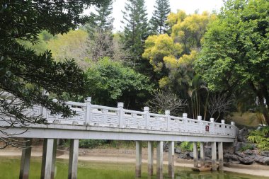 Arka planda ağaçlar olan bir su kütlesinin üzerinde bir köprü. Köprü beyaz ve üzerinde kırmızı bir işaret var.