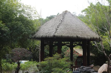 Çatı sazdan yapılmış küçük bir kulübe yemyeşil bir bahçede duruyor. Kulübe ağaçlar ve çalılarla çevrili ve yakınlarda da taş bir duvar var. Bahçe huzurlu ve sakin, sükunet hissi ile.