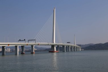 Büyük bir köprü, üzerinde açık mavi bir gökyüzü olan bir su kütlesini kapsar. Köprü bir şehirle çevrilidir ve su sakin ve hareketsizdir. Sükunet ve huzur kavramı