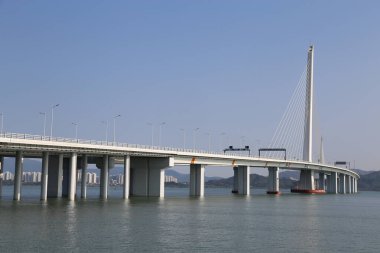 Büyük bir köprü, üzerinde açık mavi bir gökyüzü olan bir su kütlesini kapsar. Köprü yüksek binalarla çevrili ve su sakin ve durgun. Sükunet ve huzur kavramı