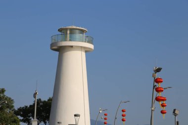 Açık mavi gökyüzü olan bir tepede bir deniz feneri var. Deniz feneri beyaz ve uzun bir kulesi var.