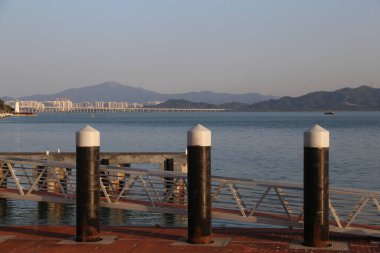 Üç siyah beyaz direk bir rıhtımın yanında suyun üzerinde duruyor. Su sakin ve gökyüzü mavi.