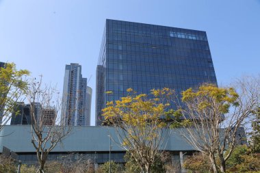 Önünde bir sürü pencere ve birkaç ağaç olan büyük bir bina. Gökyüzü açık ve mavi