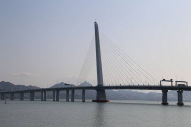 Bir köprü, üzerinde açık mavi bir gökyüzü olan bir su kütlesini kaplar. Köprü, suyun iki tarafını birbirine bağlayan büyük ve etkileyici bir yapıdır. Sahne huzurlu ve huzurlu, köprüyle
