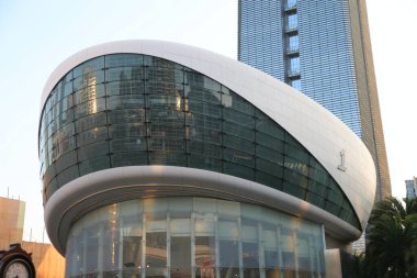 Kavisli cam cepheli büyük bir bina. Bina beyaz ve yan tarafında bir saat var.