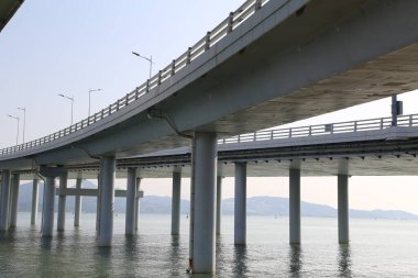 Bir köprü, üzerinde açık bir gökyüzü olan bir su kütlesini kapsar. Köprü uzun ve dar, kenarları boyunca birkaç ışık görünüyor. Su sakin ve durgun, gökyüzünü yansıtıyor.
