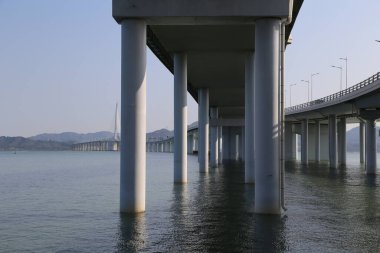Arka planda açık mavi gökyüzü olan bir su kütlesi üzerinde bir köprü. Köprü boş ve su sakin.