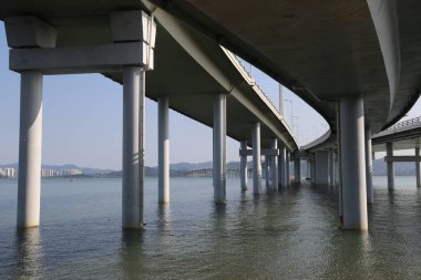 Arka planda açık mavi gökyüzü olan bir su kütlesi üzerinde bir köprü. Su sakin ve köprü boş.