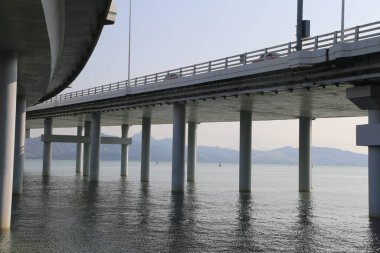 Bir köprü, üzerinde açık bir gökyüzü olan bir su kütlesini kapsar. Köprü uzun ve üzerinde birkaç araba var.