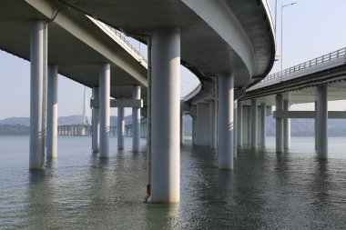 Bir köprü altında çok su bulunan geniş bir su kütlesini kapsar. Su bulanık görünüyor ve köprü tam ortasında.